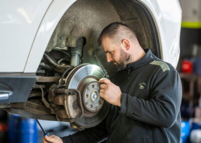 Kfz Mechaniker Arbeitet An Der Bremsanlage Eines Angehobenen Fahrzeugs In Der Werkstatt