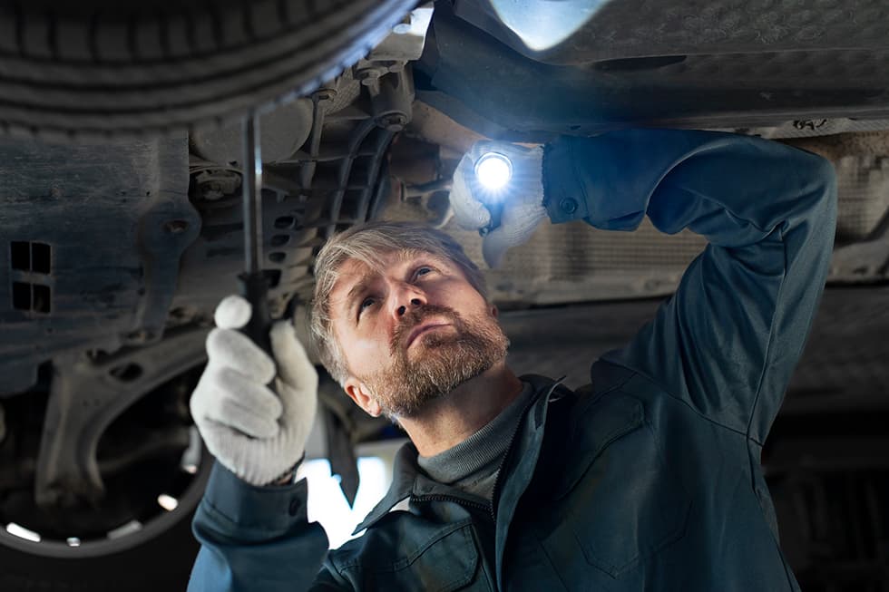 Mechaniker Untersucht Fahrwerk Unter Auto Mit Taschenlampe