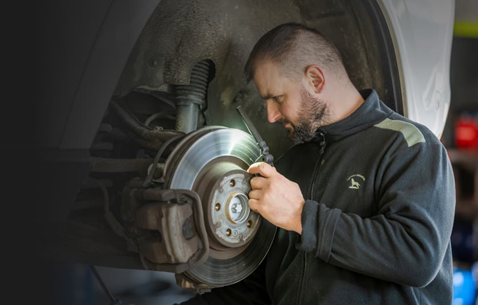 Kfz Mechaniker Arbeitet An Der Bremsanlage Eines Angehobenen Fahrzeugs In Der Werkstatt